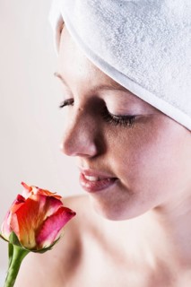 Portrait of a smiling young woman smelling a rose with a towel wrapped around her head
