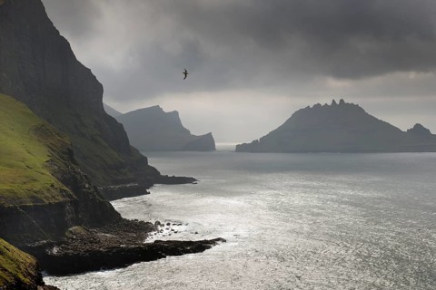 Cliffs in front of the silhouette of the rugged rocks of Tindholmur