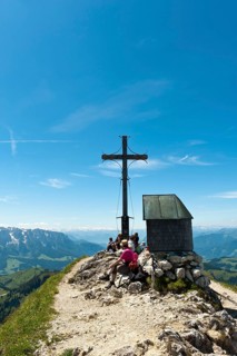 Mountain climber at the summit cross with a small chapel on Geigelstein Mountain