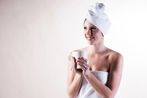 Smiling young woman with a towel wrapped around her head holding a teacup