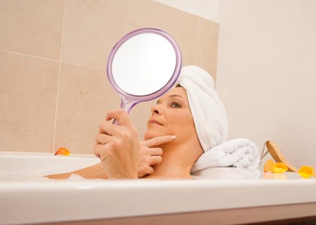 Woman taking a bath and looking at her face with a mirror