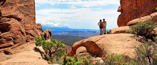 Hikers looking towards the La Sal Mountains from between red sandstone cliffs
