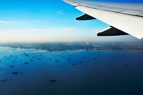 Wing of a plane and views of the port area of Jakarta on landing approach