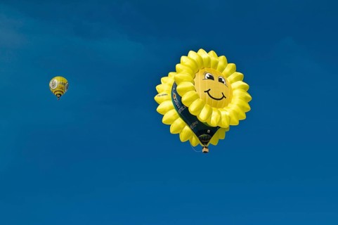 Hot air balloon in the shape of a 'laughing' sun or sunflower against a blue sky
