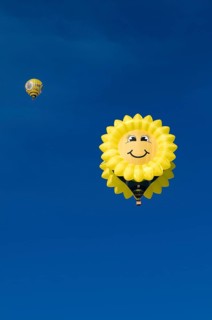 Hot air balloon in the shape of a 'laughing' sun or sunflower against a blue sky