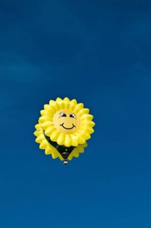 Yellow balloon with a 'smiling sun' or sunflower face against a blue sky