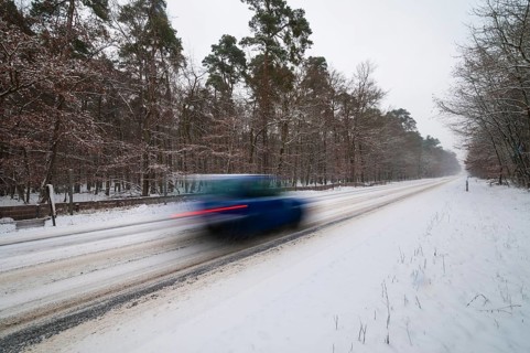 Snow-covered road in winter with car passing by quickly