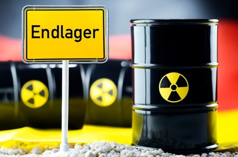 Three barrels of nuclear waste in front of a German flag and a town sign with the name 'Endlager'