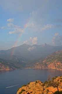 The typical bizarre red rocks of the Calanche of Piana and the mediterranean sea at the Gulf of Porto in the background below a rainbow and some clouds. The Calanche of Piana is in the western part of...