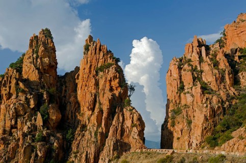 The typical bizarre red rocks of the Calanche of Piana below a blue sky and some clouds. The Calanche of Piana is in the western part of the island Corsica
