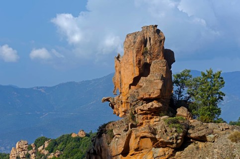 The typical bizarre red rocks of the Calanche of Piana below a blue sky and some clouds. The Calanche of Piana is in the western part of the island Corsica