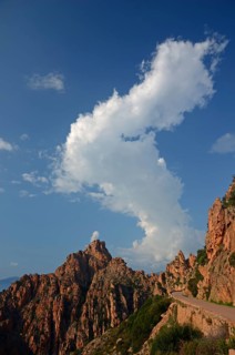 The typical bizarre red rocks of the Calanche of Piana below a blue sky and some clouds. The Calanche of Piana is in the western part of the island Corsica
