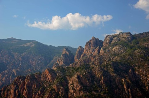 The typical rocky mountains of western Corsica near Evisa below a blue sky with a lone white cloud. Evisa illuminated by warm evening light surrounded by mountains. Evisa is in the department Corse-du...