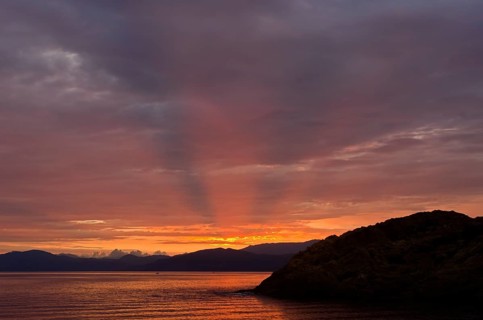 The rising sun forms sun beams behind the rocks of the island Ile de la Pietra near L'Ile-Rousse. L'Ile-Rousse is in the department Haute-Corse