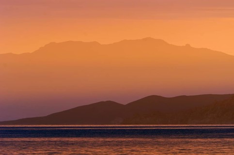 The rising sun forms sun beams behind the rocks of the island Ile de la Pietra near L'Ile-Rousse. L'Ile-Rousse is in the department Haute-Corse