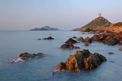 The genoese tower Tour de la Parata at the right and the islands Les Iles Sanguinaires behind the rocky mediterranean coast illuminated by warm morning light. Les Iles Sanguinaires are in the departme...