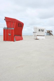 Roofed wicker beach chairs on the beach in front of a house on stilts