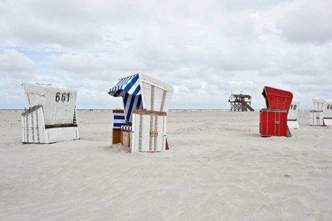 Roofed wicker beach chairs on the beach in front of a house on stilts