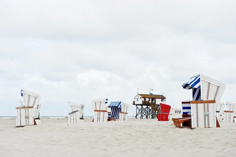 Roofed wicker beach chairs on the beach in front of a house on stilts