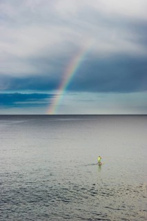 Stand up paddler with rainbow over the sea