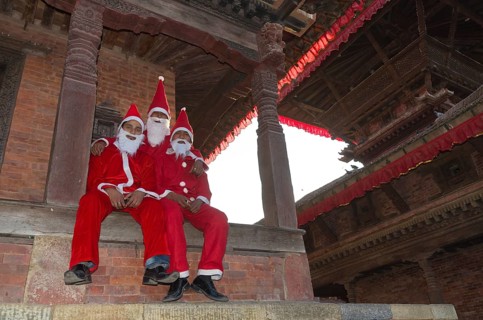 Three local men costumed as Santa Claus sitting on temple steps at Durbar Square