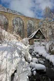 Snow-covered creek with a Black Forest house and a railway bridge