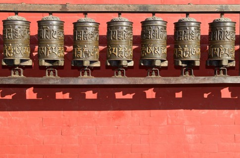 Buddhist prayer wheels in front of a red wall at Swayambhunath Stupa