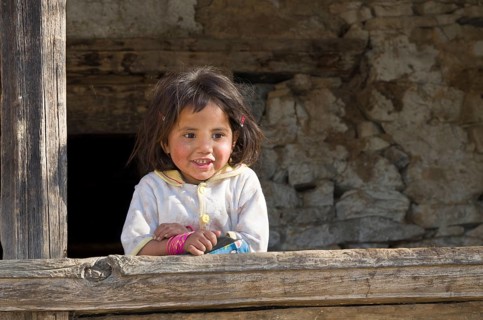 Local little girl leaning on a wooden pole