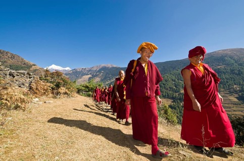 Monks and nuns wearing red cloths walking on a small path along a mountain slope
