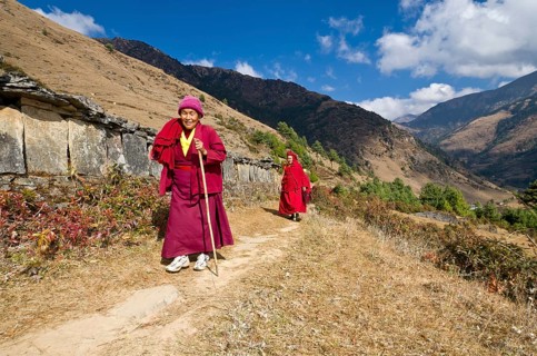 Monks and nuns wearing red cloths walking on a small path along a mountain slope