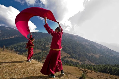 Young monks wearing red cloths flying kite with a blanket at a mountain slope