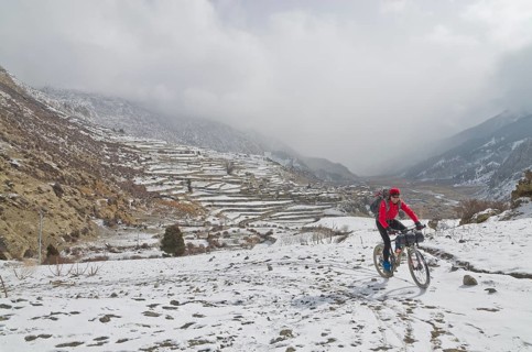 Cyclist riding his bike in the snow up towards Thorong La Pass (5416 m)