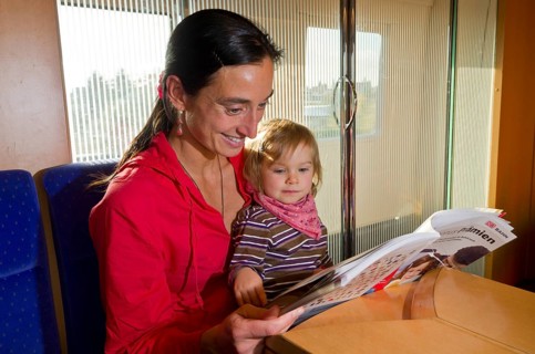 Young mother with child reading in a booklet inside ICE train