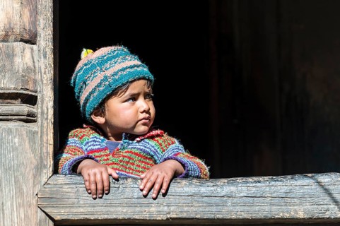A small child looking out of the window of a wooden house