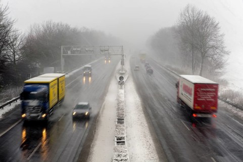 Trucks and cars on a motorway with heavy snowfall and poor visibility