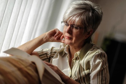Senior woman sitting at the window and reading a book