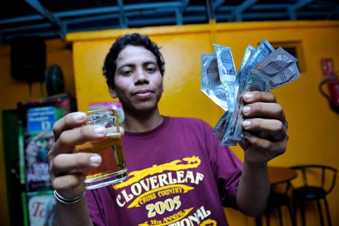 Young man in a brothel holding a beer and condoms in his hand