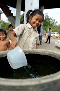 Girl drawing water from a large stone jug filled with rain water