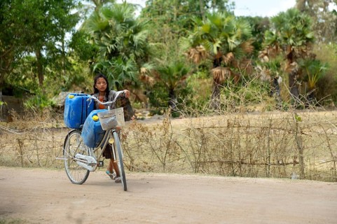 Girl transporting two canisters with water from the reservoir of the nearby pagoda on her bike to her home