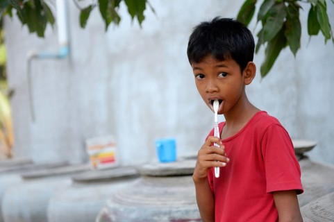 Young boy brushing his teeth outside a house