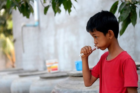 Young boy brushing his teeth outside a house
