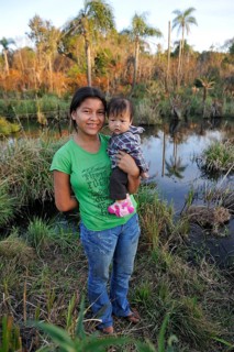 Young mother holding a child in her arms in front of a pond in the community of Mbya-Guarani Indians