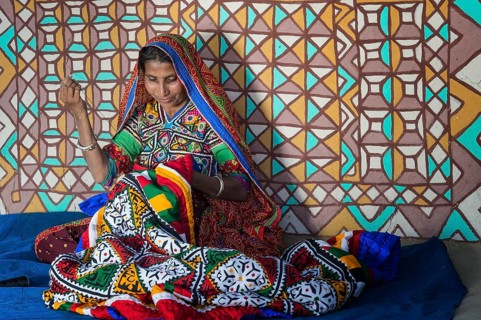 Woman in traditional clothes sewing handicraft in front of a house