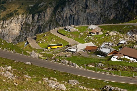 Yellow bus from the PostAuto Schweiz AG in a hamlet on the serpentine-rich Klausen Pass road