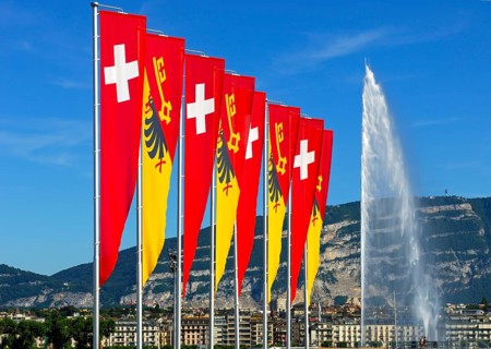 Flags of the Swiss Confederation and the Canton of Geneva on the promenade of Lake Geneva with the Jet d'Eau fountain and the summit of Saleve Mountain at the rear