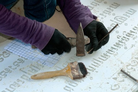 Stonemason chiselling Khmer characters into a gravestone in a stone cutting factory