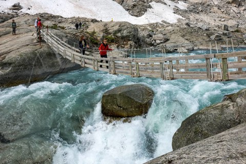 Hikers crossing a hanging bridge over a glacial river