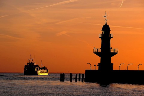 Cargo ship and silhouette of the Brunsbuttel Mole 1 lighthouse in front of a evening sky