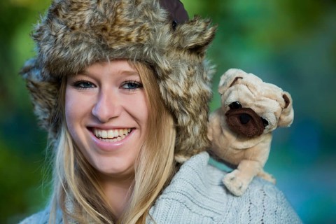 Young woman wearing a fur hat with a plush pug on her shoulder