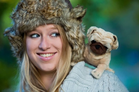 Young woman wearing a fur hat with a plush pug on her shoulder